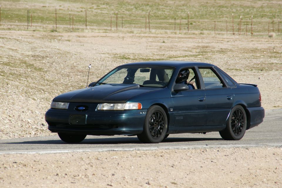 dark blue 1995 Ford Taurus on a track, driver wearing a helmet
