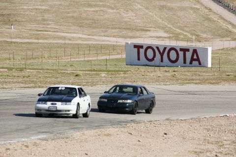 1995 Ford Taurus - Two sedans race on a track with a large TOYOTA sign in the background.