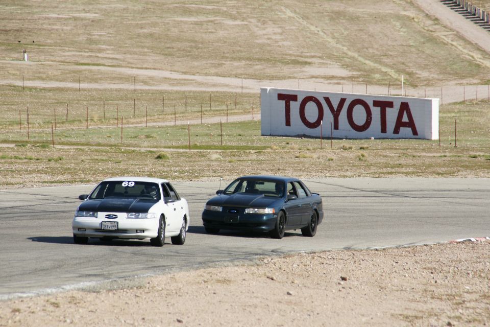 White 1995 Ford Taurus with black hood and racing number 69 on track