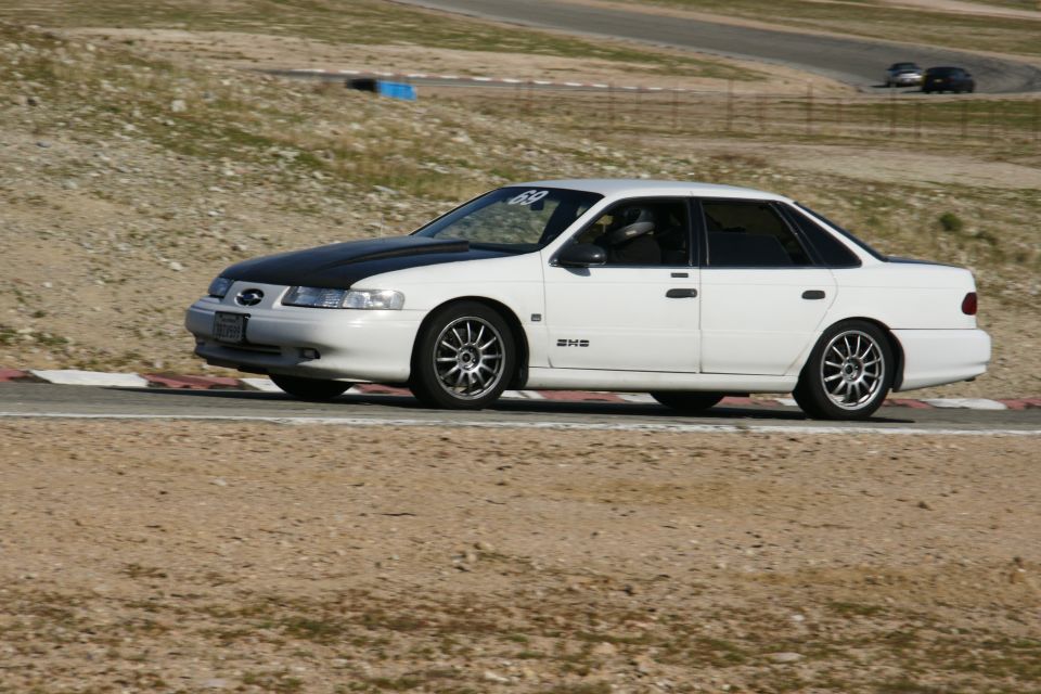 1995 Ford Taurus on a racetrack, white with black hood and aftermarket wheels