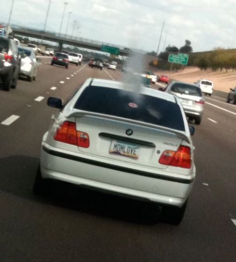 2009 Suzuki Samurai - White BMW sedan emitting smoke from its rear while driving on a busy highway.