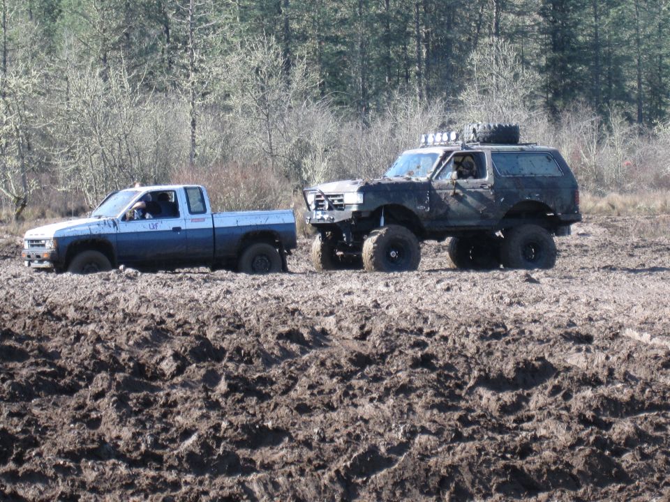 Lifted SUV on large mud tires pulling a small pickup stuck in a muddy field