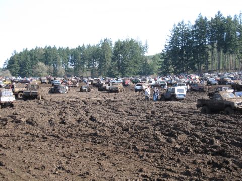 1996 Ford Bronco - A large gathering of off-road vehicles are bogged down in a muddy field during an event.