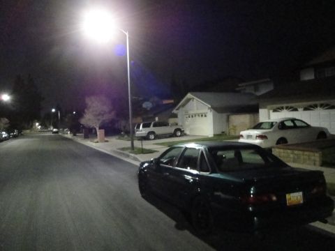 1995 Ford Taurus - A dark sedan is parked on a residential street at night under a streetlamp, with other vehicles visible in driveways.