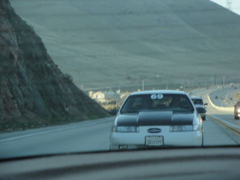 1995 Ford Taurus - 1995 Ford Taurus with racing number 69 on highway, other cars visible in background.