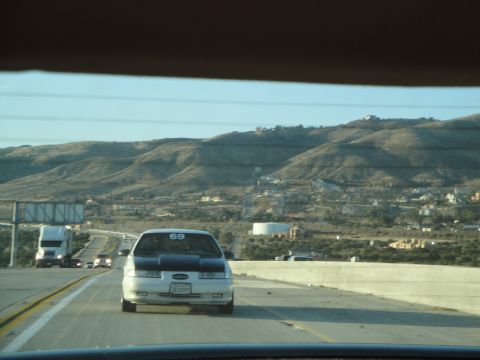 1995 Ford Taurus - A white sedan with a contrasting black hood and the number 69 displayed on its windshield travels down a highway, with a semi-truck visible…