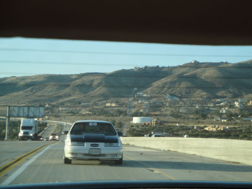 White sedan with black hood, racing number 69 on windshield, driving on highway