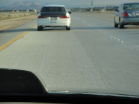 1995 Ford Taurus - A white sedan with a black hood is seen from behind on a highway, with another car to the right.