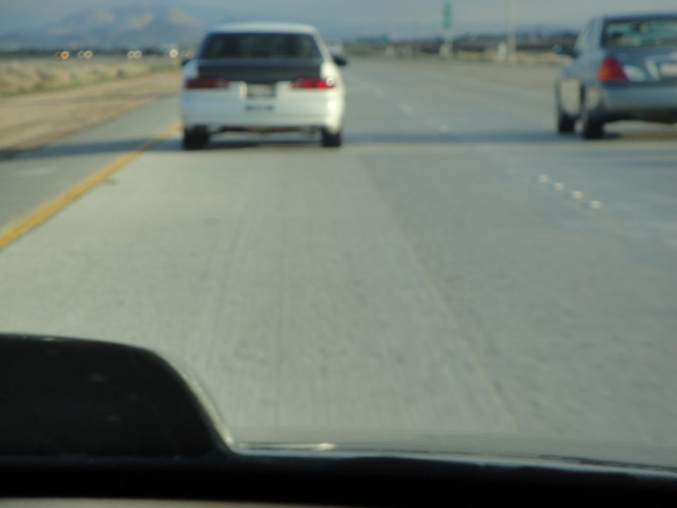 White sedan with a black hood driving on a highway, rear view