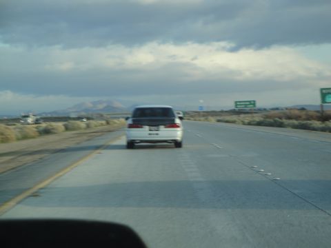 1995 Ford Taurus - A white 1995 Ford Taurus drives down a highway under a cloudy sky.