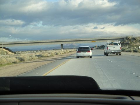 1995 Ford Taurus - Two vehicles travel down a highway under a bridge, with mountains in the distance.