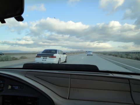 1995 Ford Taurus - A white sedan with a black trunk lid travels down a highway under a cloudy sky.
