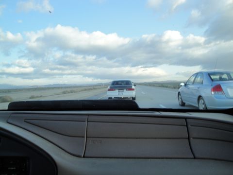 1995 Ford Taurus - Two cars drive down a highway under a cloudy sky.