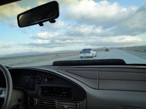 1995 Ford Taurus - A white sedan with a black roof drives down a highway under a cloudy sky.