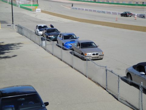 1995 Ford Taurus - A tan BMW 3 Series sedan is parked alongside a race track, with several other vehicles visible in the scene.