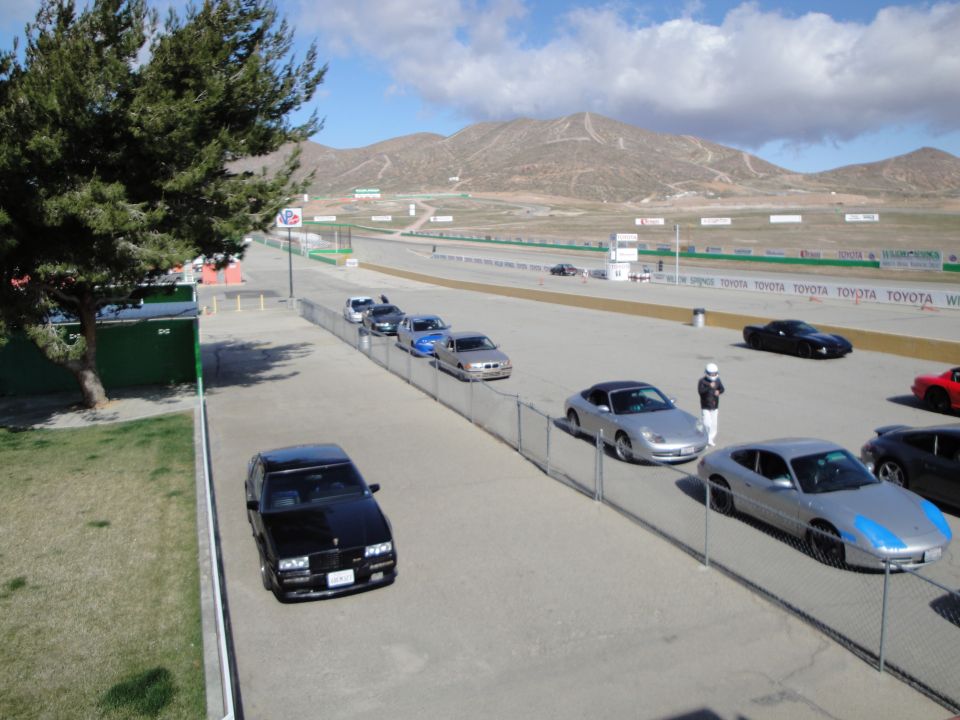 Race track with several cars parked along the side and one on the track; mountains in background