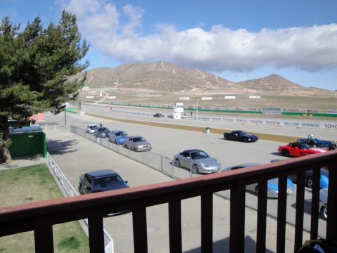 1995 Ford Taurus - Cars are parked along the side of a race track under a partly cloudy sky.