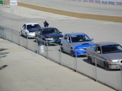 1995 Ford Taurus - Multiple cars, including a Subaru WRX and a BMW, line up on a race track with track signage in the background.