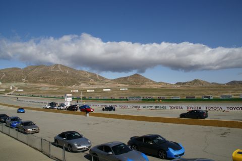 1995 Ford Taurus - Several sports cars are lined up on the asphalt at Willow Springs International Raceway under a cloudy sky.