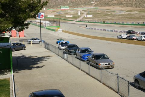 1995 Ford Taurus - A line of cars waits on the pit lane of a race track, with spectators and mountains visible in the distance.