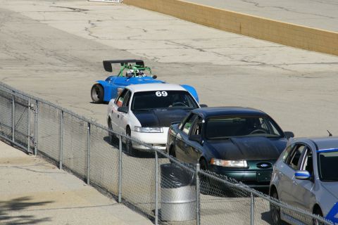 1995 Ford Taurus - A white sedan with a black hood and racing number 69 is seen on a track alongside other vehicles.