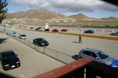 1995 Ford Taurus - Multiple vehicles are seen on a racetrack under a cloudy sky with mountains in the distance.