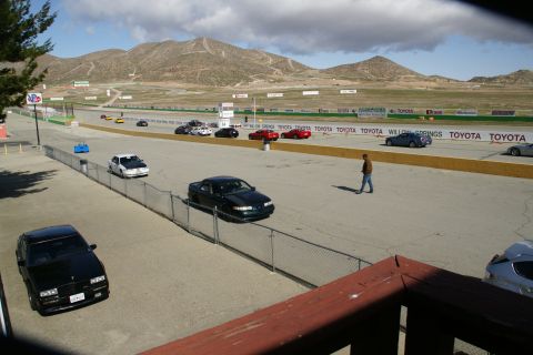 1995 Ford Taurus - A dark sedan is on the race track at Willow Springs with other vehicles and mountains in the distance.
