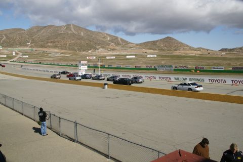 1995 Ford Taurus - Multiple cars are on the Willow Springs race track under a cloudy sky.