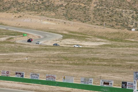 1995 Ford Taurus - Several cars are driving on a winding race track in a dry, hilly landscape.