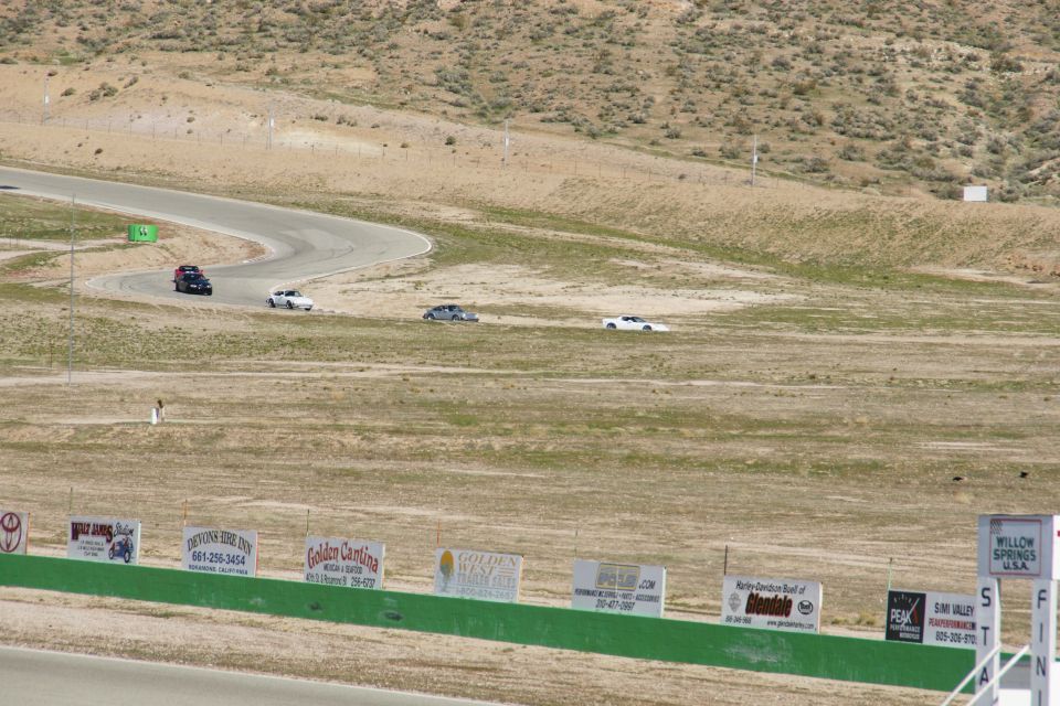 Cars on a race track with dry, hilly terrain and advertising signs