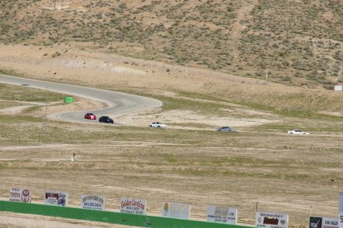1995 Ford Taurus - Multiple vehicles are seen on a winding race track under a dry, hilly landscape.