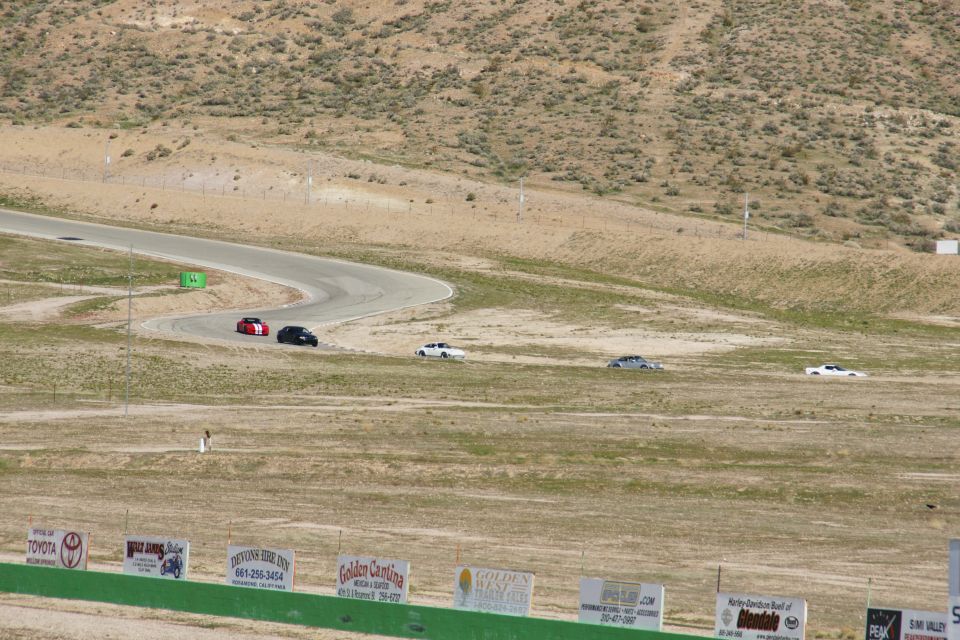 Cars on a race track with dry hills and signs in the foreground