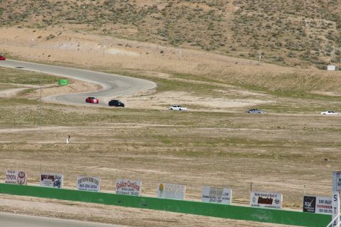 1995 Ford Taurus - Several cars are driving on a race track, with a dry, hilly landscape surrounding the course.