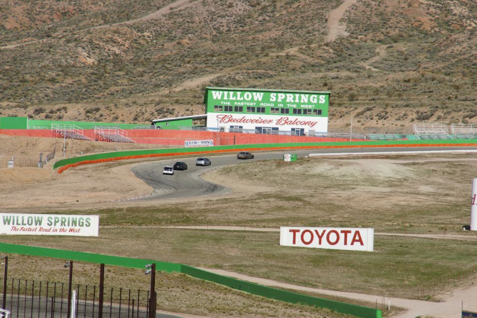 Cars race on a track with Willow Springs building in background