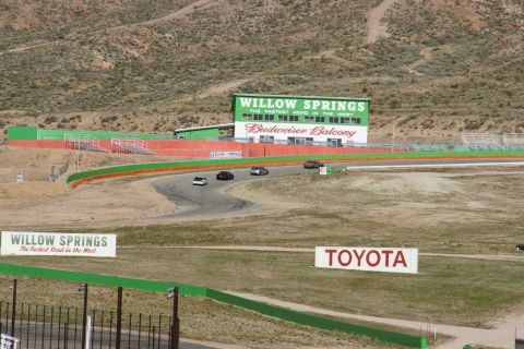 1995 Ford Taurus - Several cars are driving on a winding race track with the Willow Springs International Raceway building visible.