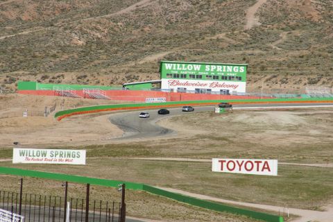 1995 Ford Taurus - Several cars race on a track at Willow Springs International Raceway, with the Budweiser Balcony building visible.