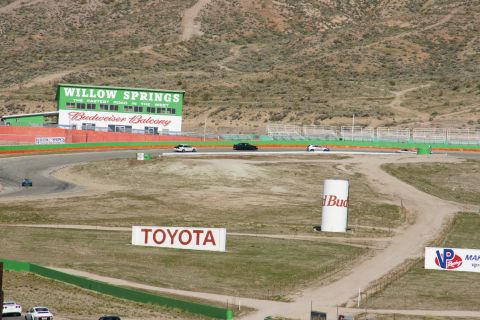 1995 Ford Taurus - View of Willow Springs Raceway, showing the Budweiser Balcony and a Toyota sign, with cars on the track.