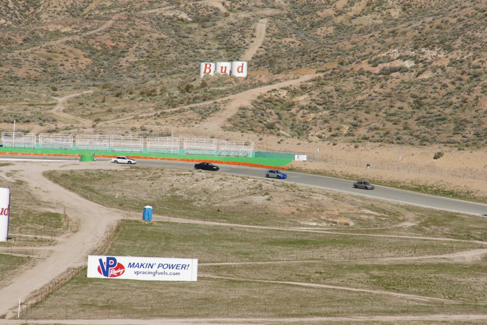 Race track with several cars driving, Budweiser sign on hill, VP Racing Fuels banner
