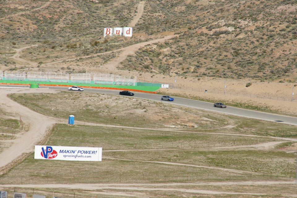 Cars on a race track with a Budweiser sign on the hill and a VP Fuels banner