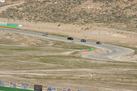 1995 Ford Taurus - Multiple vehicles are seen on a winding race track under a bright sky, with sparse vegetation and distant hills.
