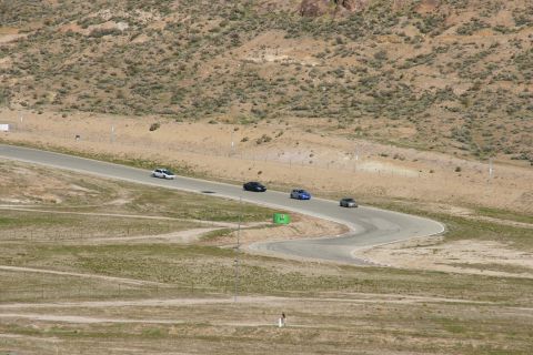 1995 Ford Taurus - Multiple vehicles navigate a turn on a race track surrounded by arid hills.