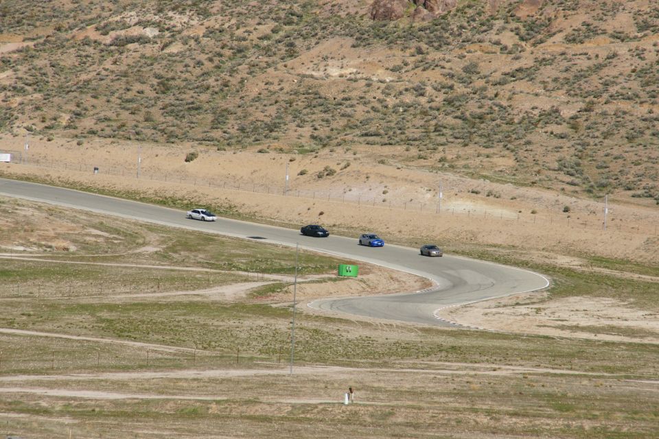Four cars driving on a winding asphalt racetrack with dry, hilly terrain in the background
