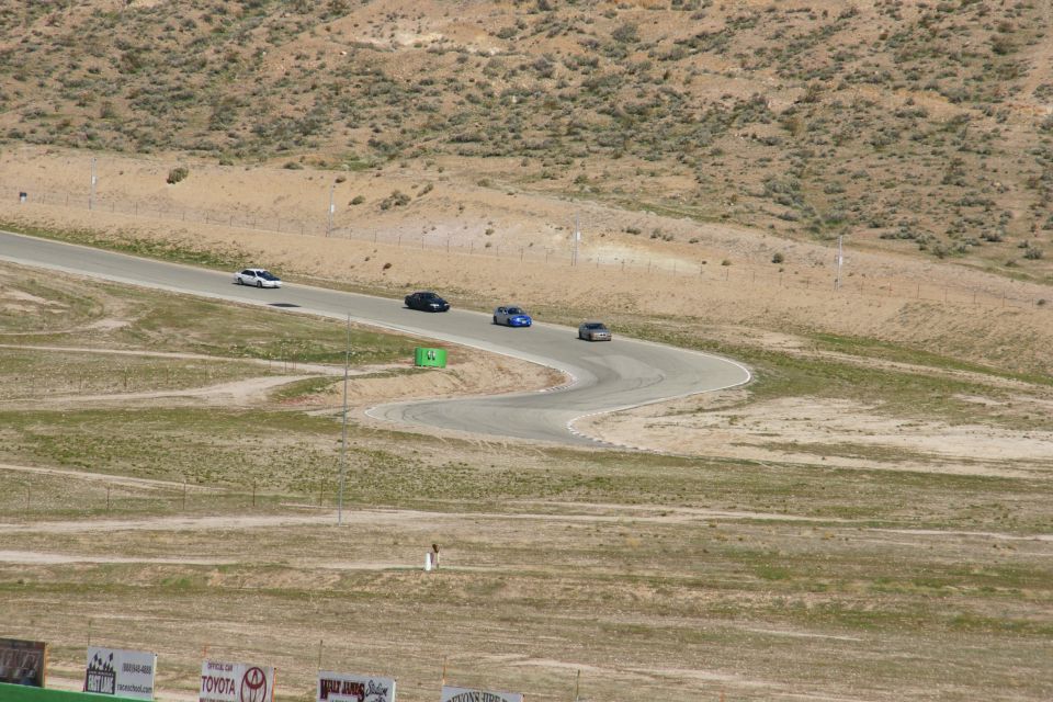 Four cars race on a winding asphalt track in a dry, hilly landscape