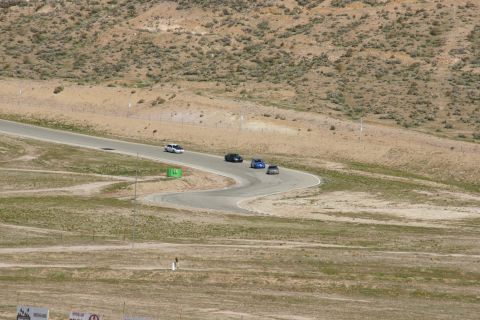 1995 Ford Taurus - Several cars are navigating a curve on a race track with arid hills in the background.