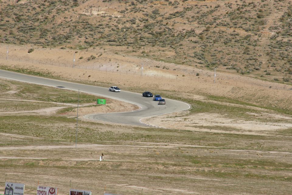Cars on a winding racetrack with dry, hilly terrain