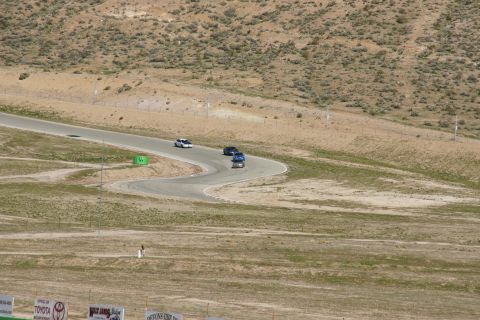 1995 Ford Taurus - Multiple vehicles navigate a turn on a race track surrounded by arid hills.