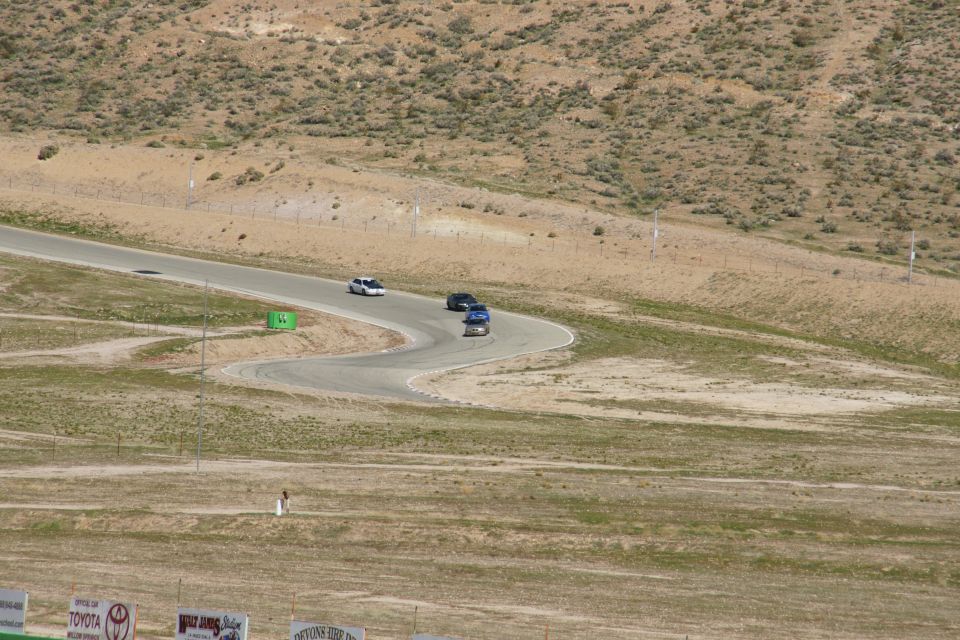 Three cars on a winding race track with dry, hilly terrain