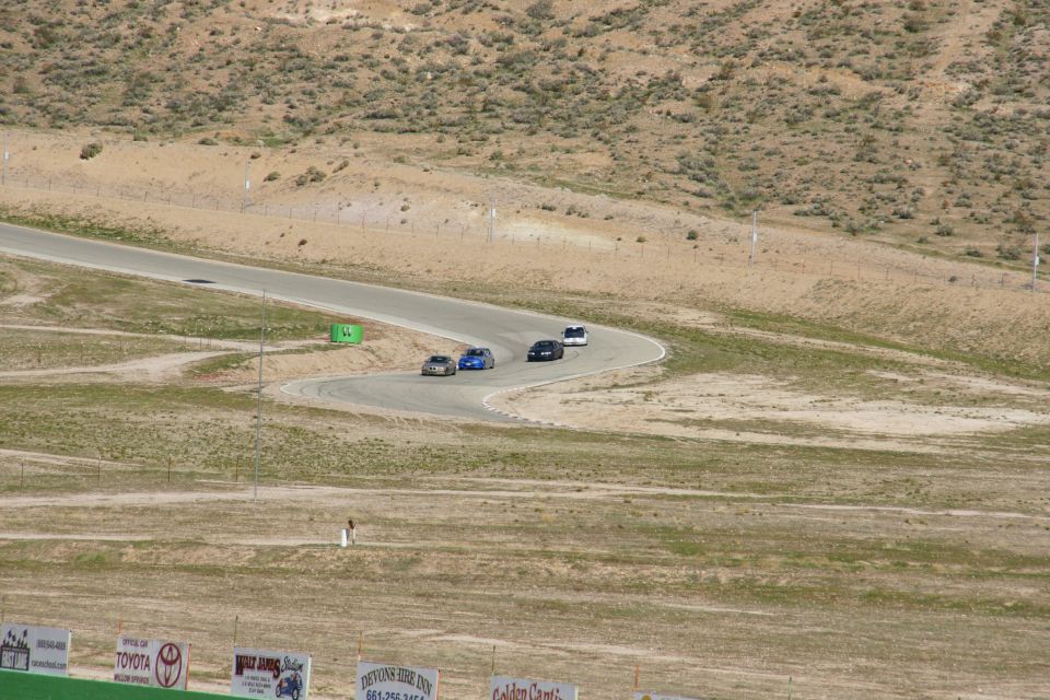 Several cars are driving on a winding race track in a desert landscape