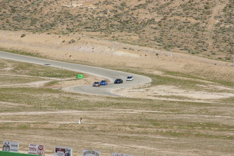 Several cars race on a winding track with dry, hilly terrain