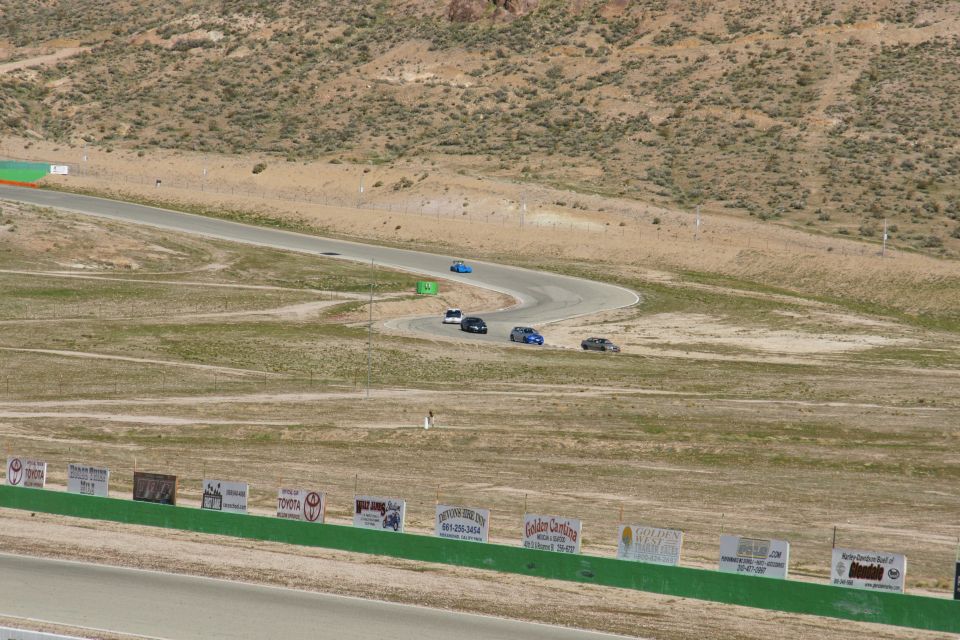 Cars on a winding race track with desert hills and sponsor signs